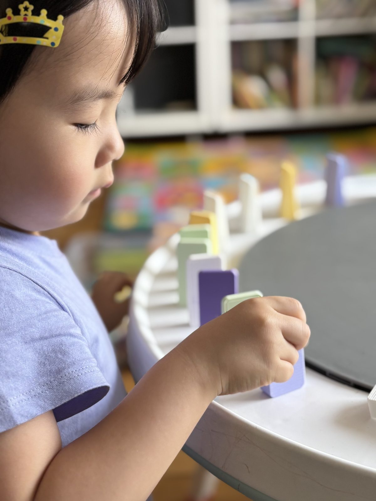 A close-up of a child's hand carefully balancing an EZ Domino piece